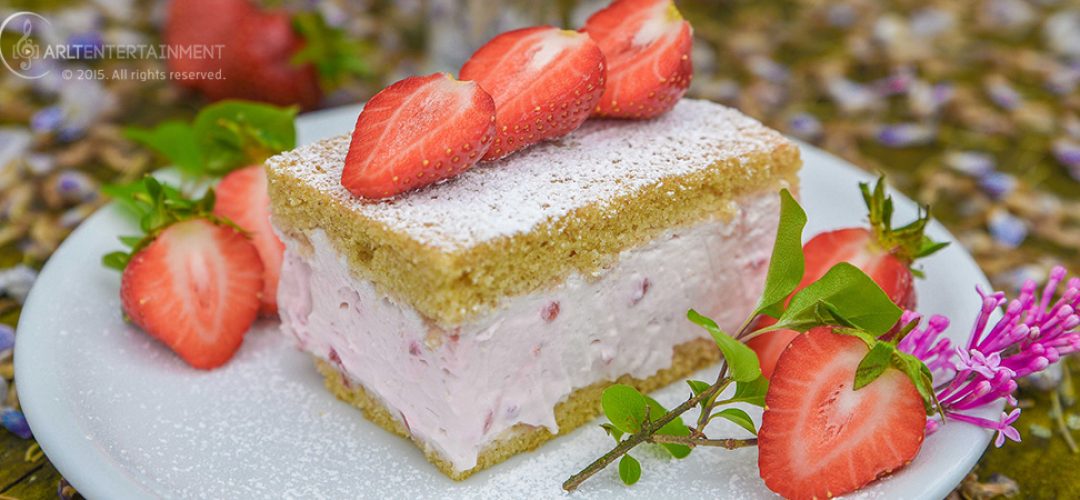 ErdbeerkäseSahne Torte auf einem weißßen Teller mit Flieder und Erdbeeren
